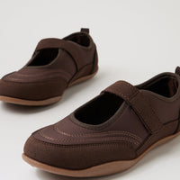 A pair of dark brown slip-on shoes with hook-and-loop straps and tan soles, photographed on a clean white studio background.